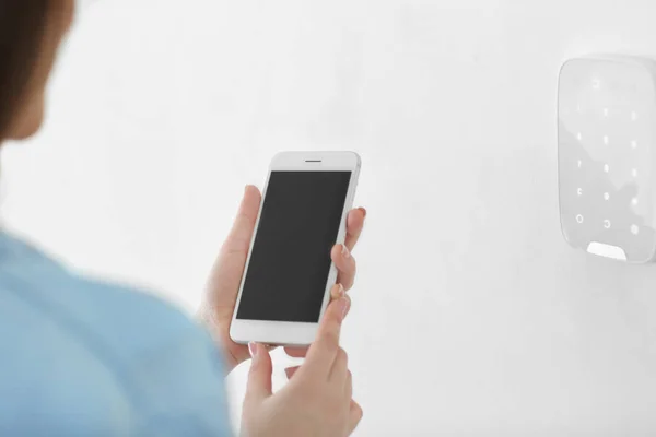 Young woman with phone near security system indoors