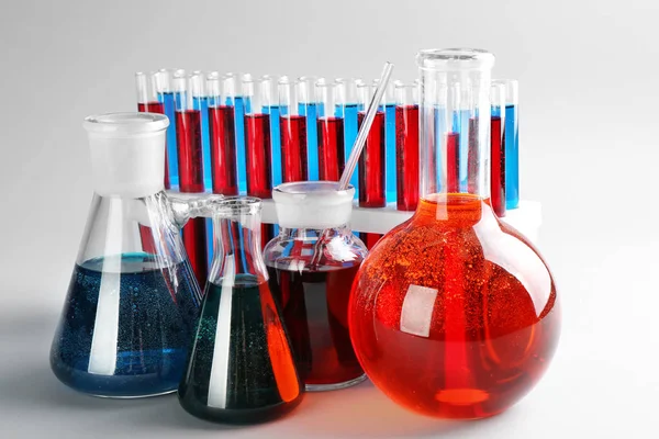 Wyroby ze szkła chemiko z płynami kolorowe na jasnym tle — Zdjęcie stockowe