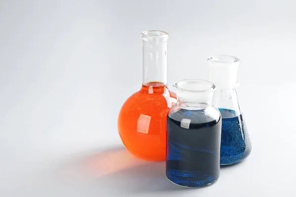 Хімічний скляний посуд з барвистими рідинами на світлому фоні — стокове фото