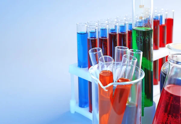 Хімічний скляний посуд з різними рідинами на кольоровому фоні — стокове фото