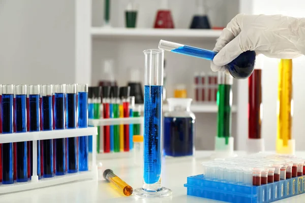 Travailleur de laboratoire versant du liquide bleu dans le tube à essai sur la table — Photo