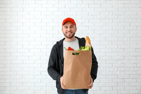 レンガの紙袋の商品と若い男は壁の背景です。食品の配達サービス — ストック写真