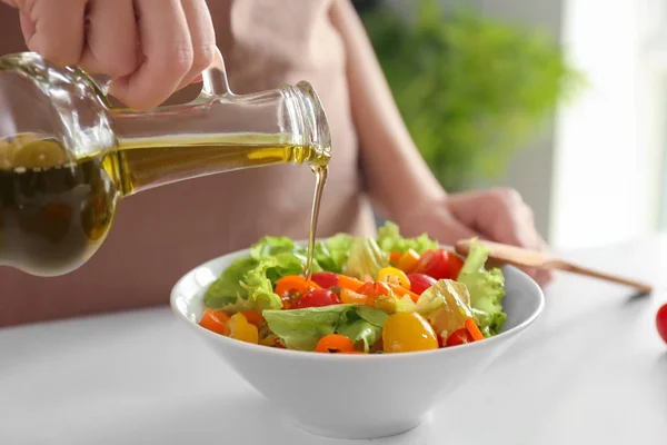 Vrouw toevoegen van olijfolie in de kom met verse fruit salade op tafel — Stockfoto