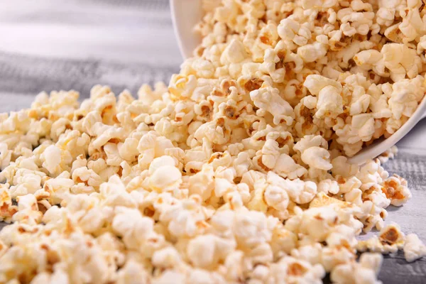 Paper bucket with scattered tasty popcorn on table, closeup — Stock Photo, Image