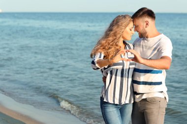 Sevimli genç bir çift deniz kıyısında kendi elleriyle kalp yapma