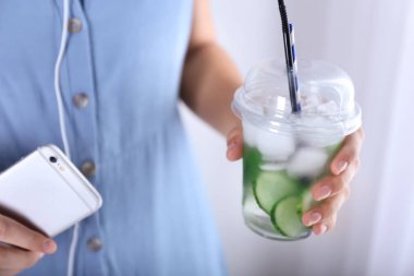 Lezzetli taze salatalık suyu ve cep telefonu, closeup ile plastik bardak tutan kadın