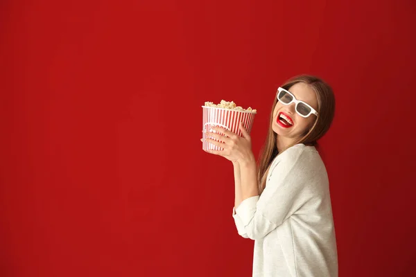 Beautiful young woman with cup of popcorn and 3D cinema glasses on color background — Stock Photo, Image
