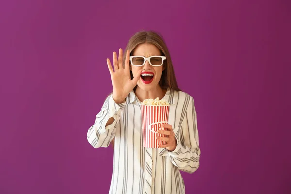 Emotional young woman with cup of popcorn and 3D cinema glasses on color background — Stock Photo, Image
