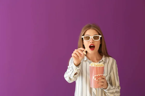 Mujer joven emocional con copa de palomitas de maíz y gafas de cine 3D sobre fondo de color — Foto de Stock