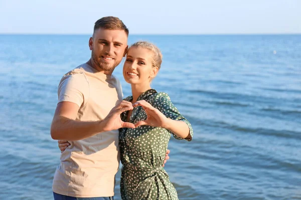 Schattig jong koppel maken hart met hun handen op de kust — Stockfoto