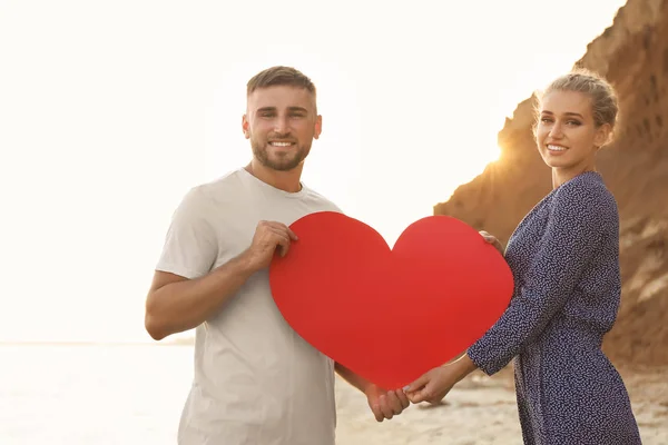 Cute young couple with red heart on sea shore — Stock Photo, Image