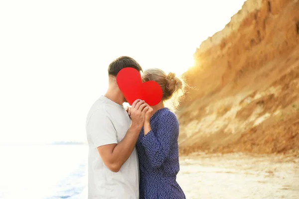 Linda pareja joven con corazón rojo en la orilla del mar — Foto de Stock