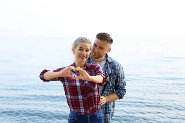 Cute young couple making heart with their hands on sea shore — Stock Photo, Image