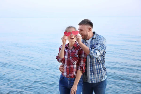 Funny young couple with red hearts on sea shore — Stock Photo, Image