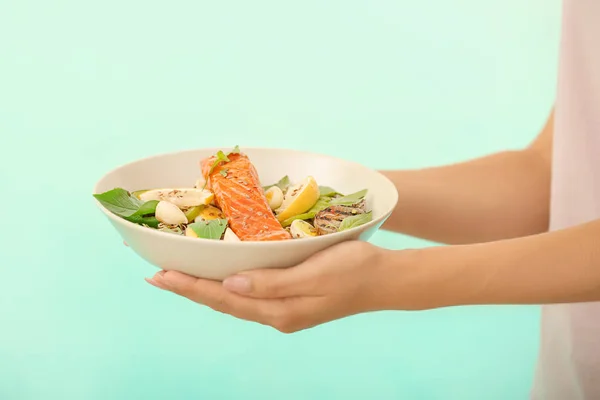 Женщина держит тарелку с вкусным лососем и свежим салатом на цветном фоне — стоковое фото
