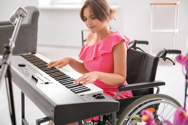 Beautiful young musician in wheelchair playing synthesizer at home — Stock Photo, Image