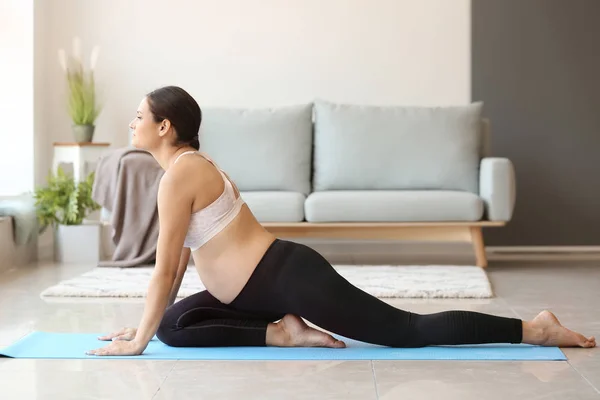 Ung gravid kvinna som utövar yoga hemma — Stockfoto