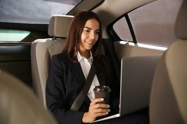 Jovem empresária com laptop beber café no carro — Fotografia de Stock