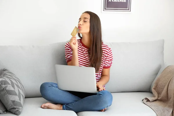 Jovem feliz com cartão de crédito e laptop após compras on-line em casa — Fotografia de Stock