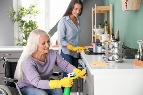 Mulher madura na cozinha de limpeza de cadeira de rodas, juntamente com a filha — Fotografia de Stock