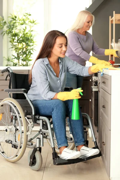 Mladá žena ve vozíku a její matka, úklid kuchyně — Stock fotografie