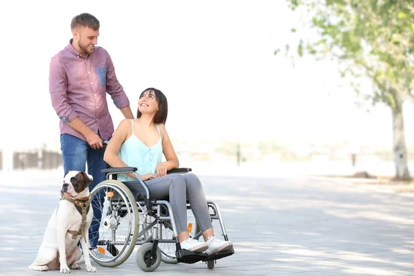 Young woman in wheelchair with her husband and service dog outdoors — Stock Photo, Image