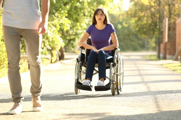 Woman in wheelchair looking at healthy person outdoors — Stock Photo, Image