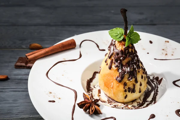 Plate with tasty baked pear and chocolate sauce on wooden table — Stock Photo, Image