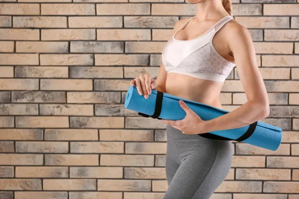 Sporty young woman holding yoga mat near brick wall — Stock Photo, Image