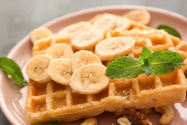Delicious waffles with banana slices and nuts on plate, closeup