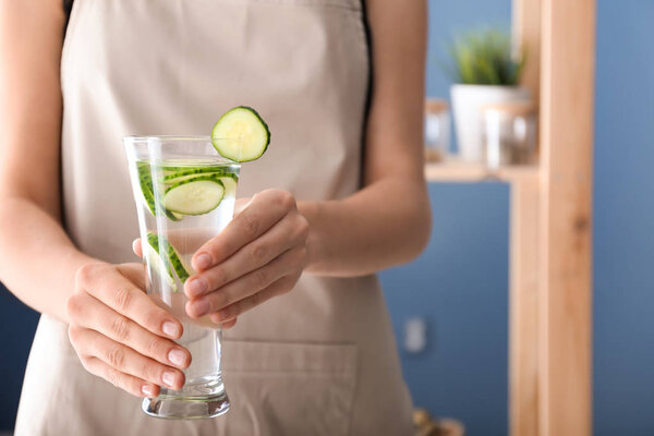 Woman holding glass with tasty fresh cucumber water indoors