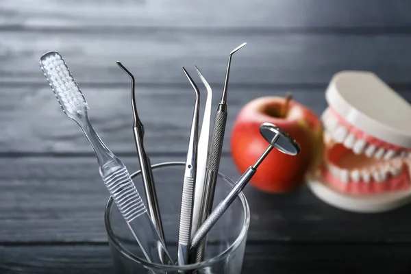 Verre avec brosse à dents et instruments dentaires sur table en bois sombre — Photo