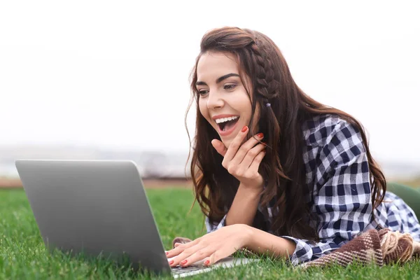 Joyeux jeune femme avec ordinateur portable reposant sur l'herbe verte à l'extérieur — Photo