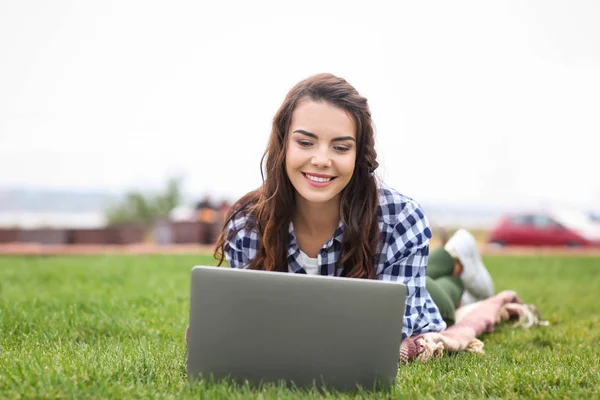 Joyeux jeune femme avec ordinateur portable reposant sur l'herbe verte à l'extérieur — Photo