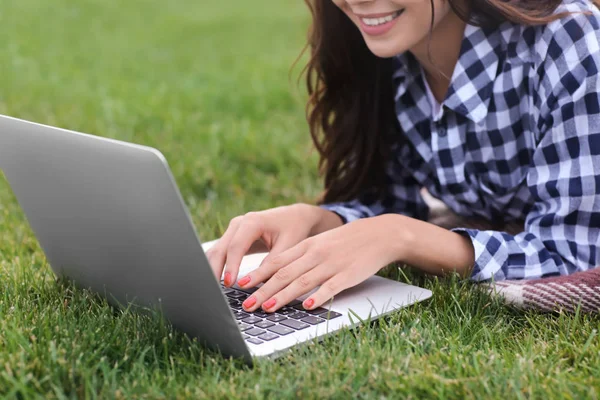 Joyeux jeune femme avec ordinateur portable reposant sur l'herbe verte à l'extérieur — Photo