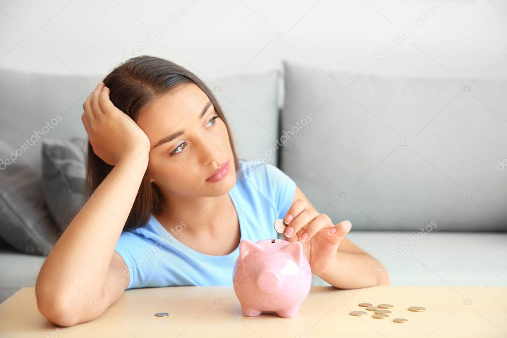 Sad young woman with piggy bank at home