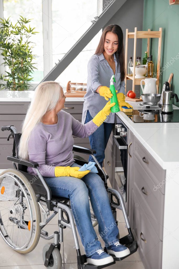Mature woman in wheelchair cleaning kitchen together with daughter