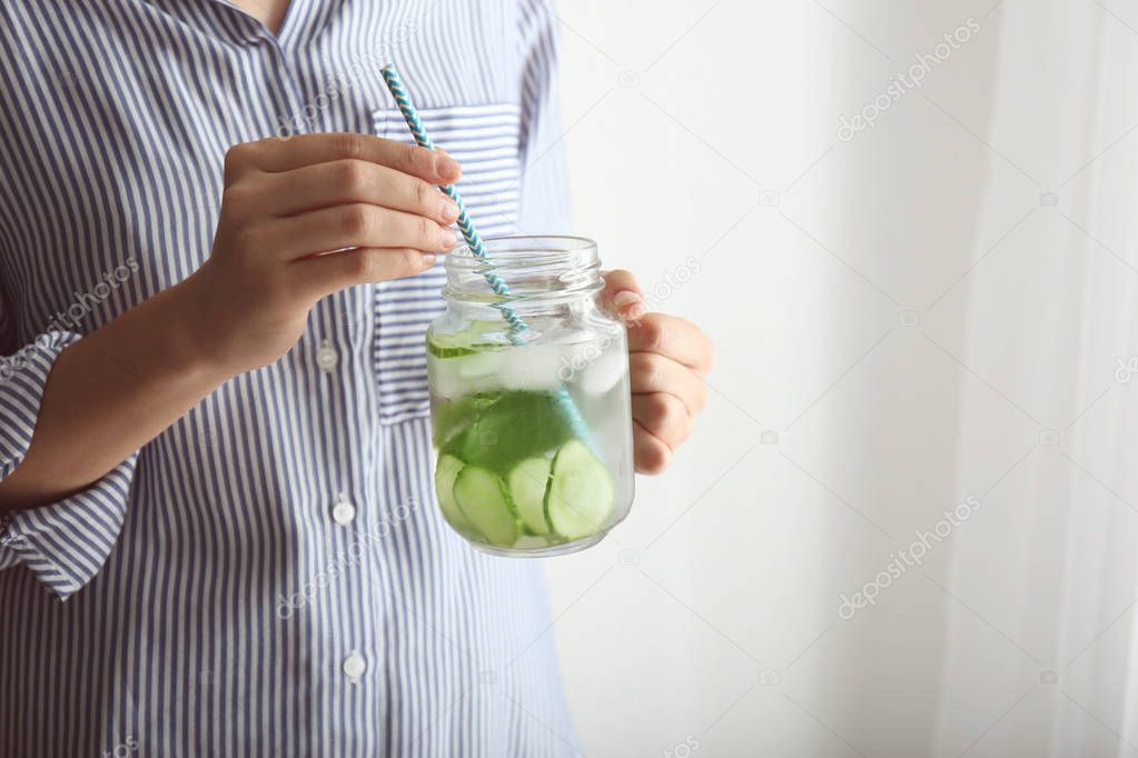 Woman holding mason jar with tasty fresh cucumber water