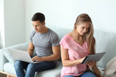 Evde kanepede otururken dizüstü ve tablet bilgisayar ile genç çift