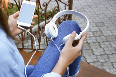 Hareket eden telefon ve kulaklık açık havada merdivenlerde oturan genç kadınla