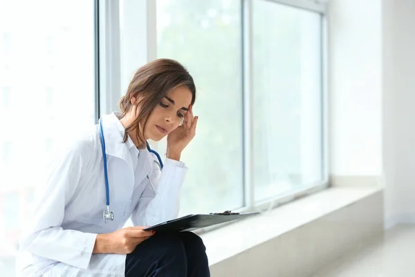Tired female doctor sitting on windowsill in her office — Stock Photo, Image