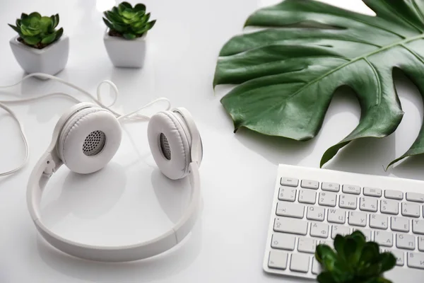 Słuchawki z komputera klawiatura i tropikalny liść na biały stół — Zdjęcie stockowe