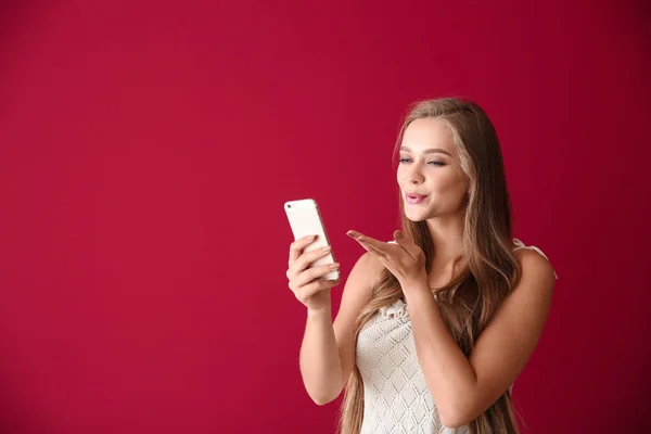 Young woman with mobile phone having online dating on color background — Stock Photo, Image