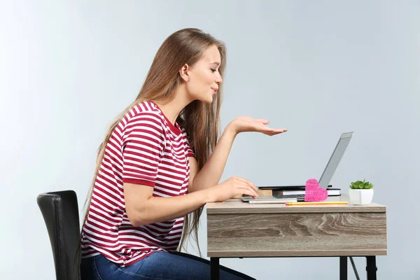 Молода жінка має знайомства онлайн, сидячи за столом з ноутбуком на сірому фоні — стокове фото