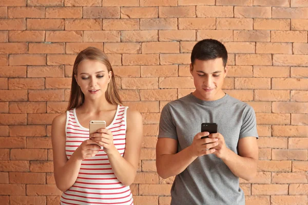 Young couple with mobile phones against brick wall — Stock Photo, Image