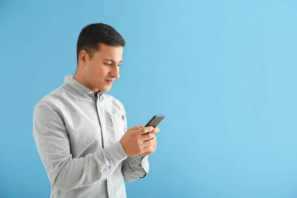 Young man with mobile phone on color background — Stock Photo, Image