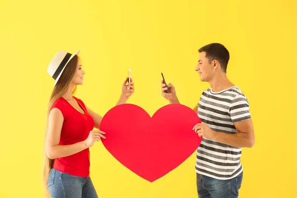 Young couple with mobile phones and big paper heart on color background — Stock Photo, Image