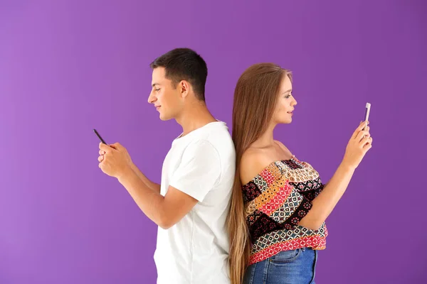 Young couple with mobile phones on color background — Stock Photo, Image