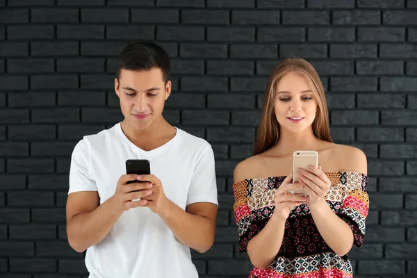 Young couple with mobile phones against brick wall — Stock Photo, Image