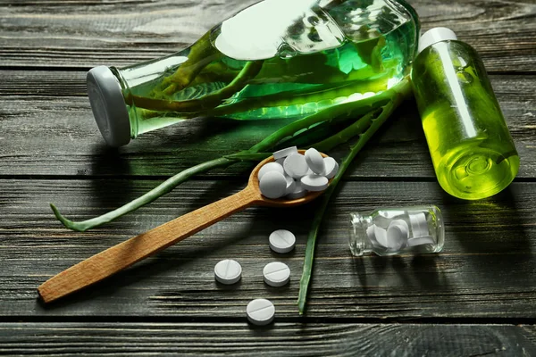 Garrafas de óleo essencial com pílulas e aloe vera na mesa de madeira — Fotografia de Stock